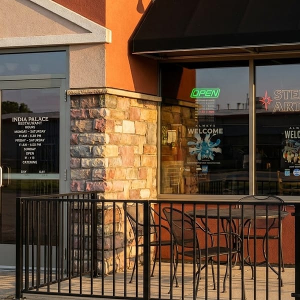 Exterior of India Palace Restaurant with a black awning, stone facade, and outdoor seating.