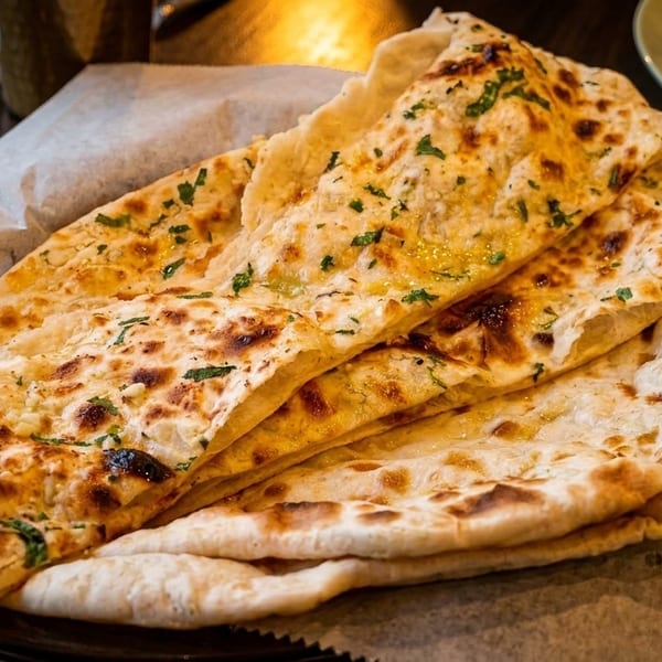 Basket of freshly baked naan bread, some topped with garlic and herbs, on a restaurant table.