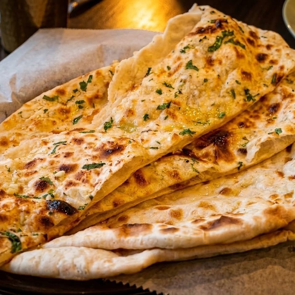 Basket of freshly baked naan bread, some topped with garlic and herbs, on a restaurant table.