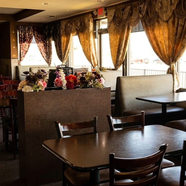 Empty restaurant dining room with dark wood tables, upholstered booths, and ornate golden curtains.