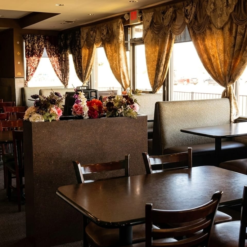 Empty restaurant dining room with dark wood tables, upholstered booths, and ornate golden curtains.